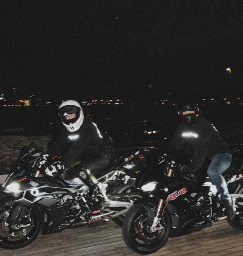 Two motorcyclists on their bikes at night with city lights in the background