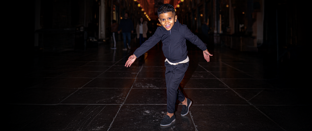 Child in dark clothing standing on a dark tiled floor with a blurred background